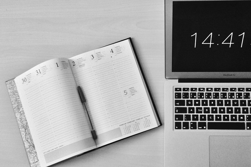 book next to laptop with time
